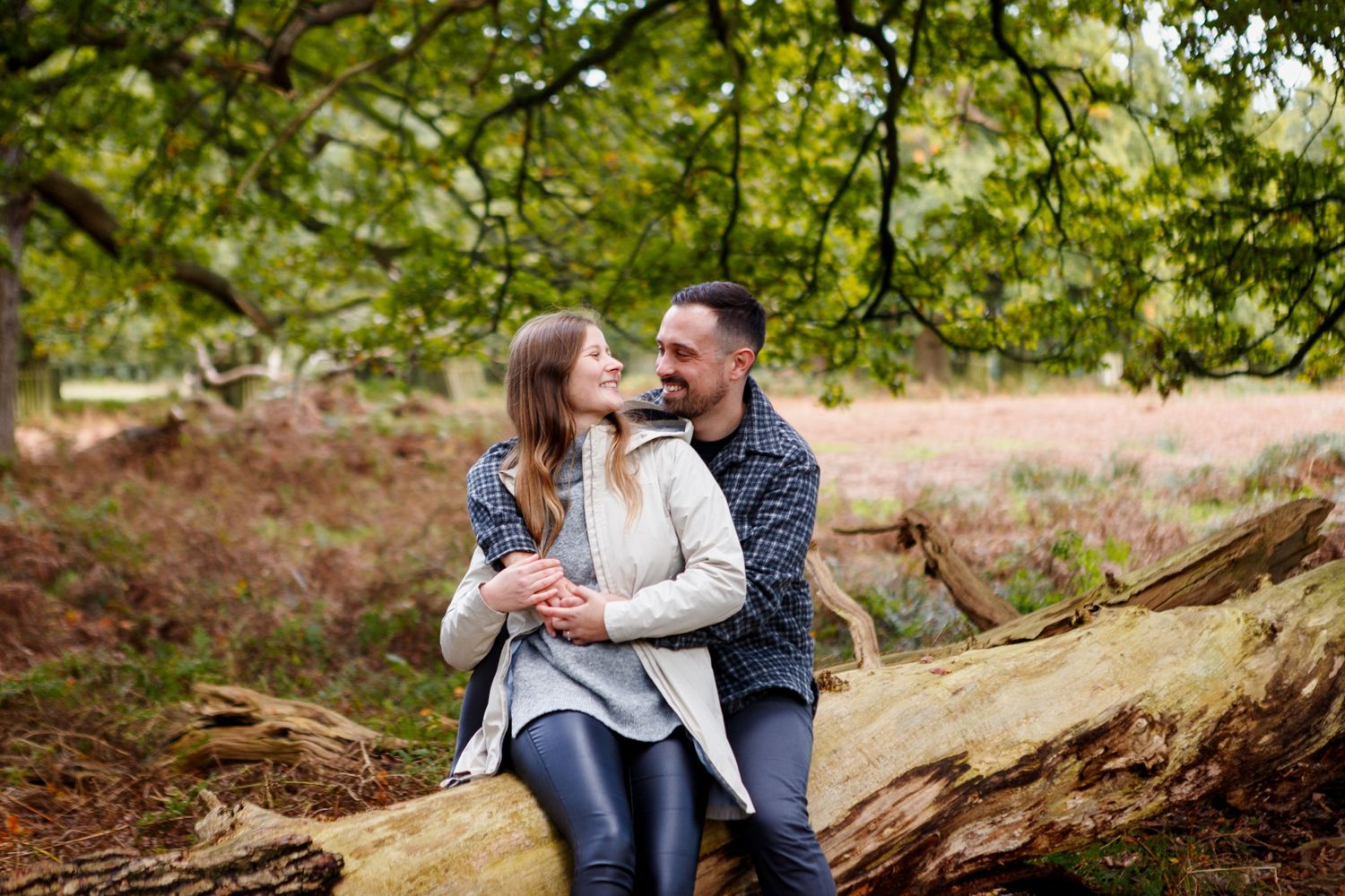 A couple shares a tender moment while sitting on a fallen tree in an autumn forest.