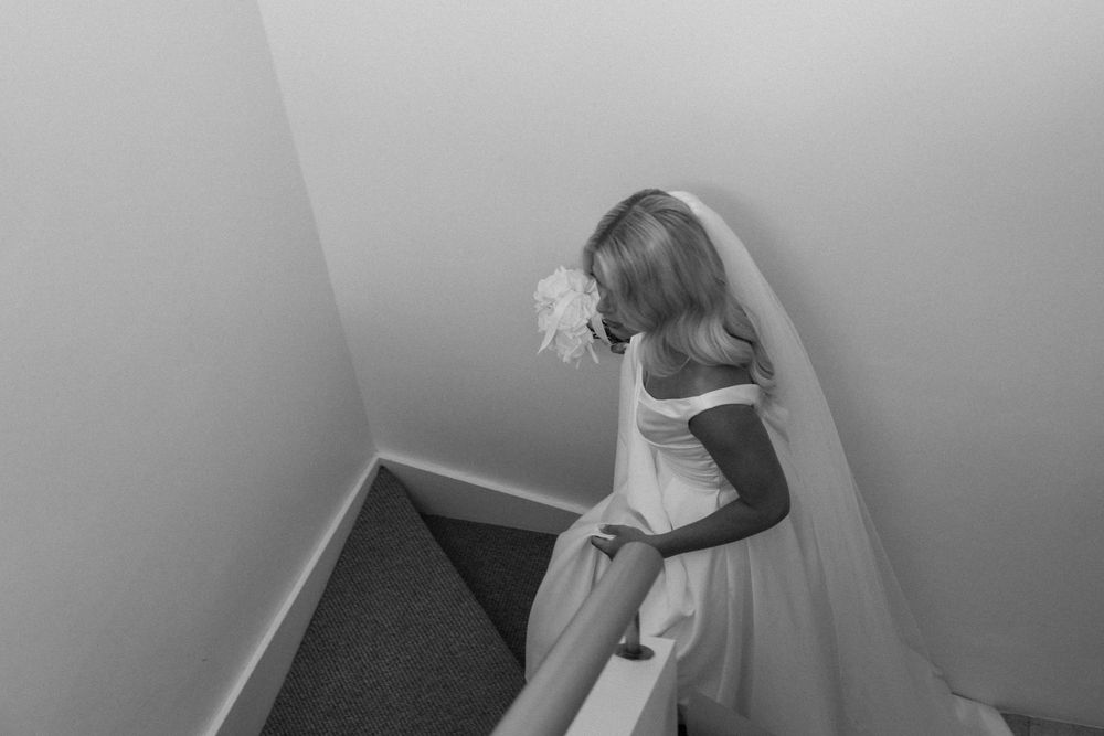 Black and white photo of a bride in a white gown and veil descending a staircase on her wedding day.