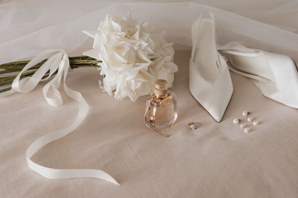 Elegant bridal flat lay with white hydrangea bouquet, perfume bottle, pearl earrings, and ivory heels on linen.