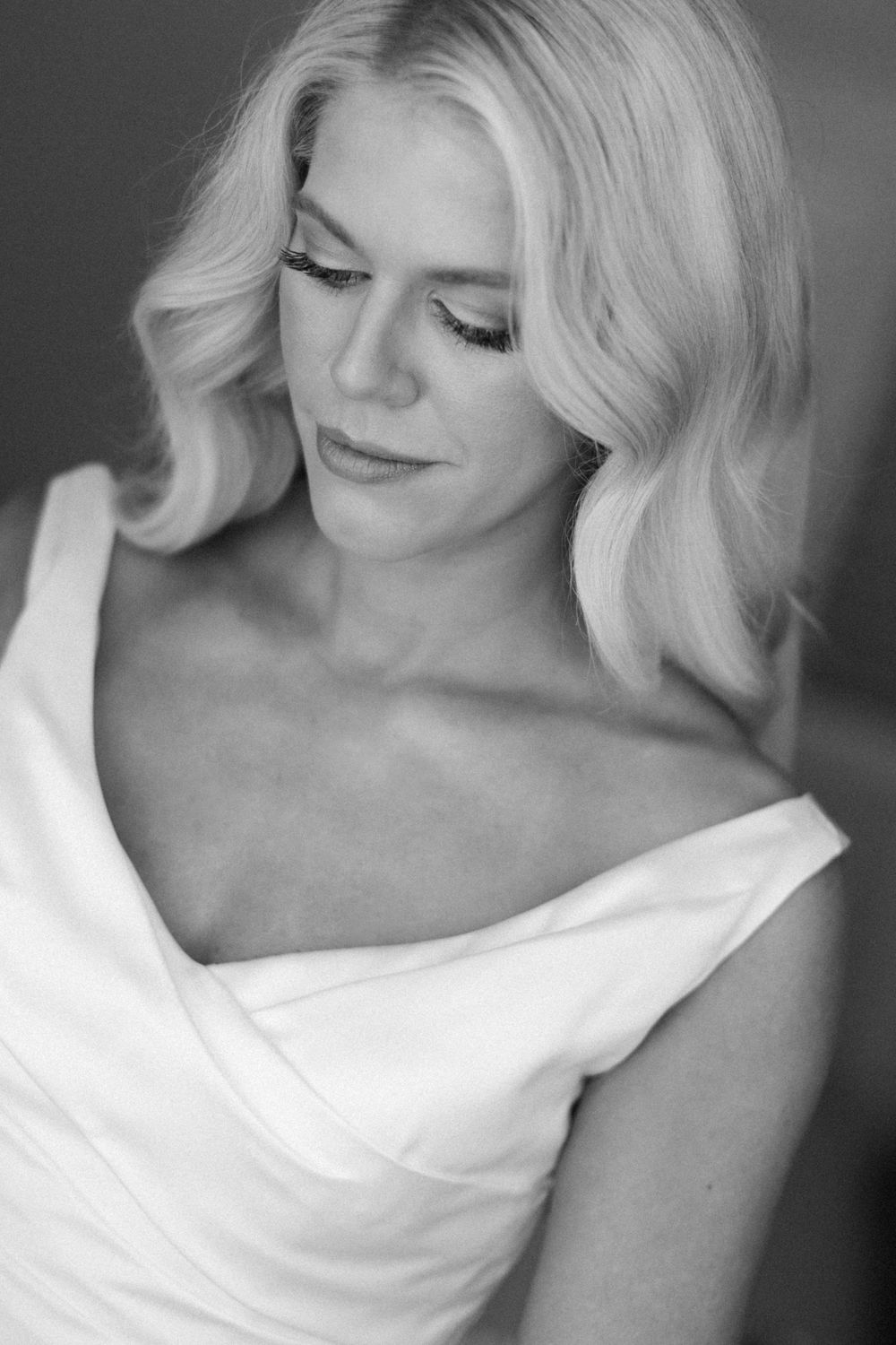 Black and white portrait of a blonde woman in a white dress, looking down gracefully.