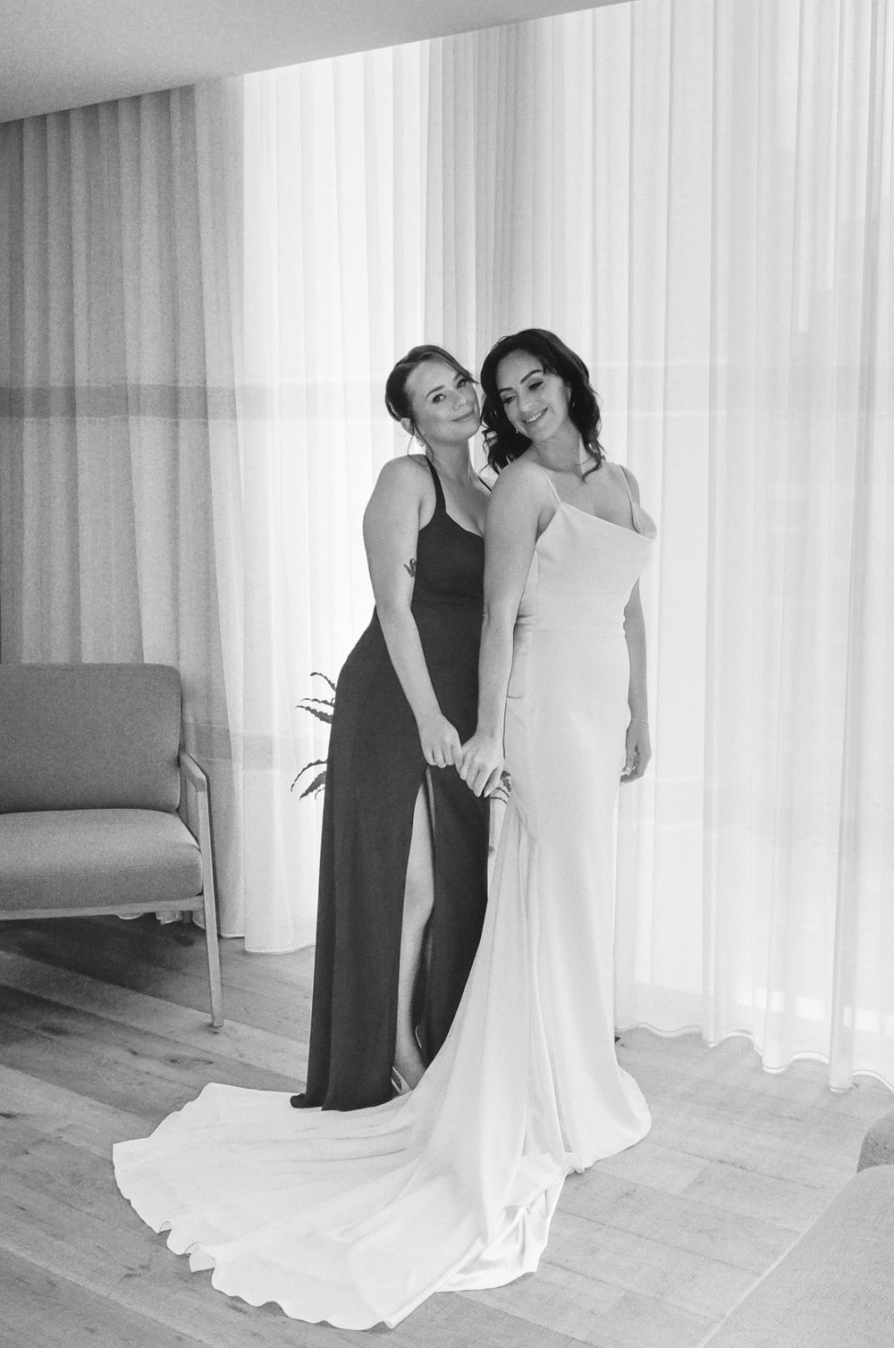 Bride and bridesmaid pose together in elegant gowns, captured in a timeless black and white wedding portrait.