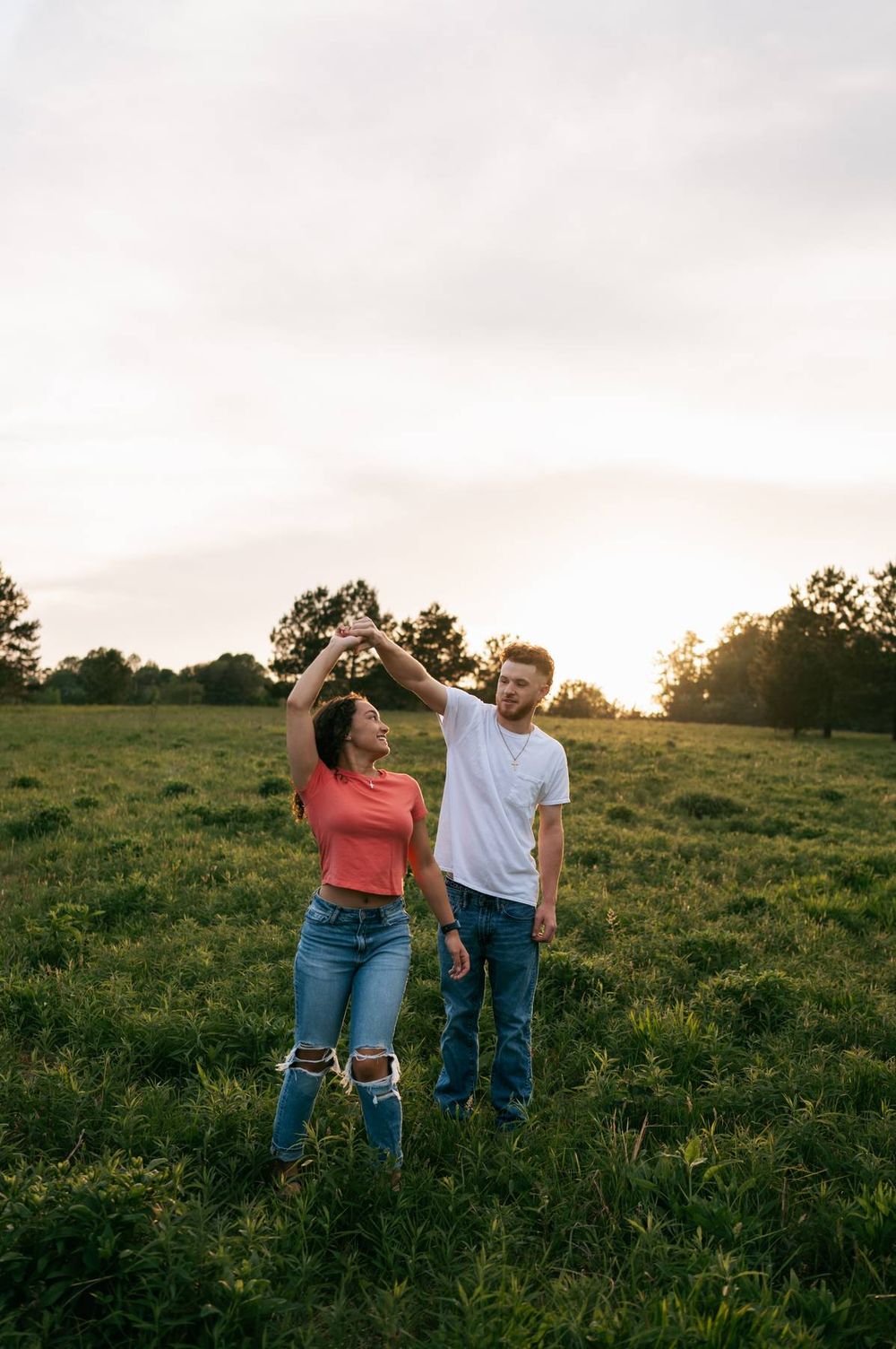 Couple dancing together in a sunlit green field at sunset, woman spinning under mans raised hand, couples photographer Greensboro NC