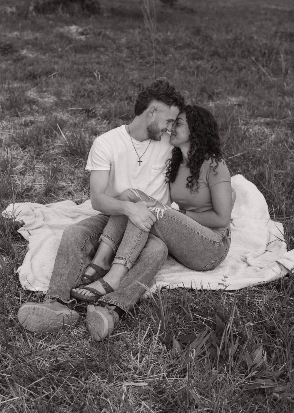 Black and white photo of a couple sitting on a blanket in a field, leaning in for a kiss Lexington NC