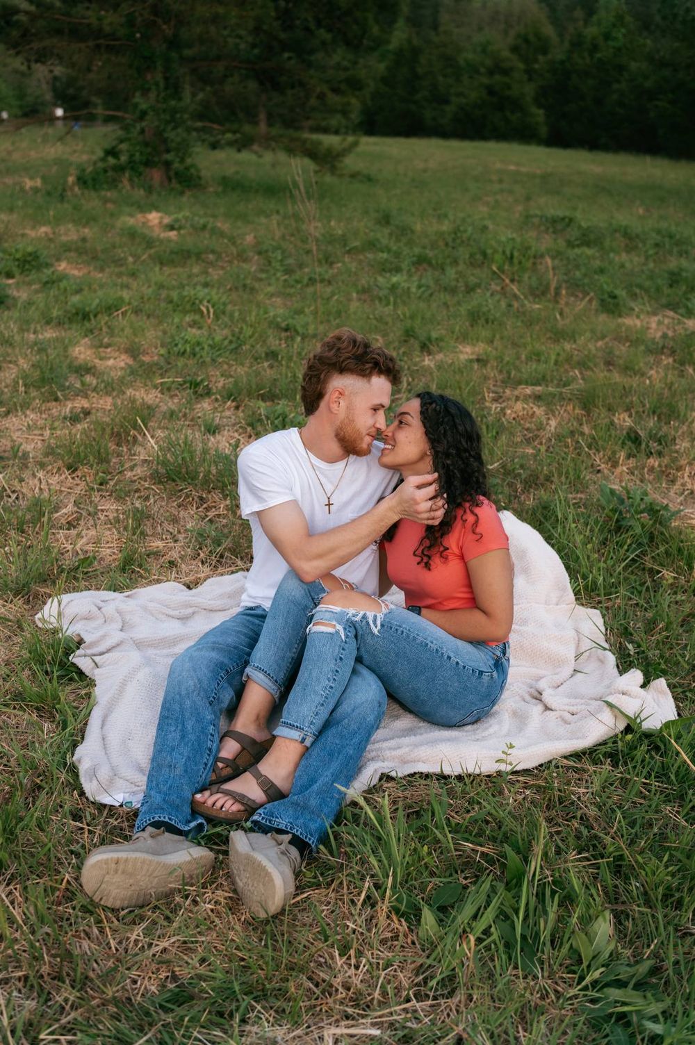 Romantic couple sitting on a blanket in a green field, sharing a tender moment together High Point NC