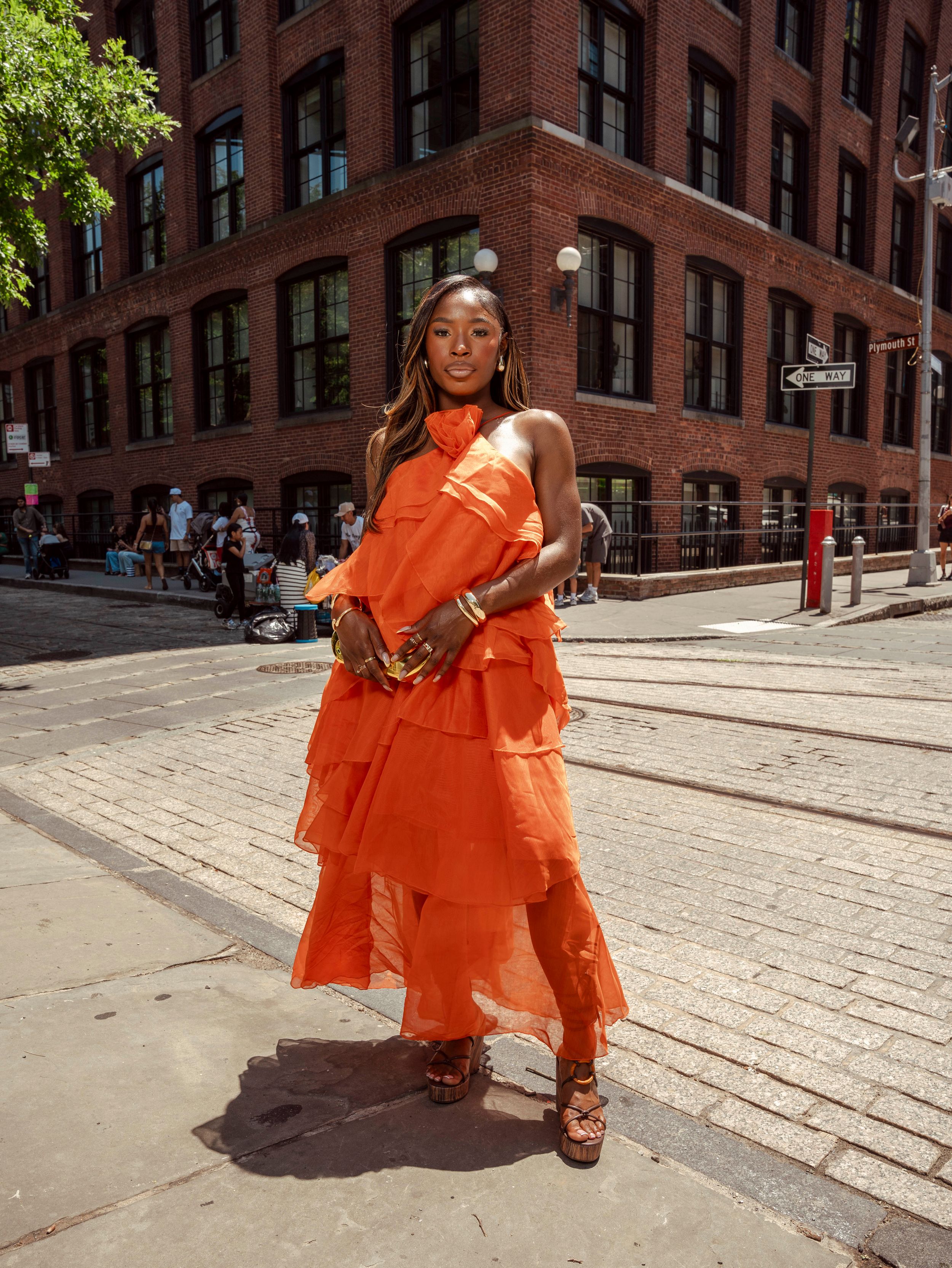 Stylish woman in bright orange tiered halter maxi dress posing on sunny NYC street.