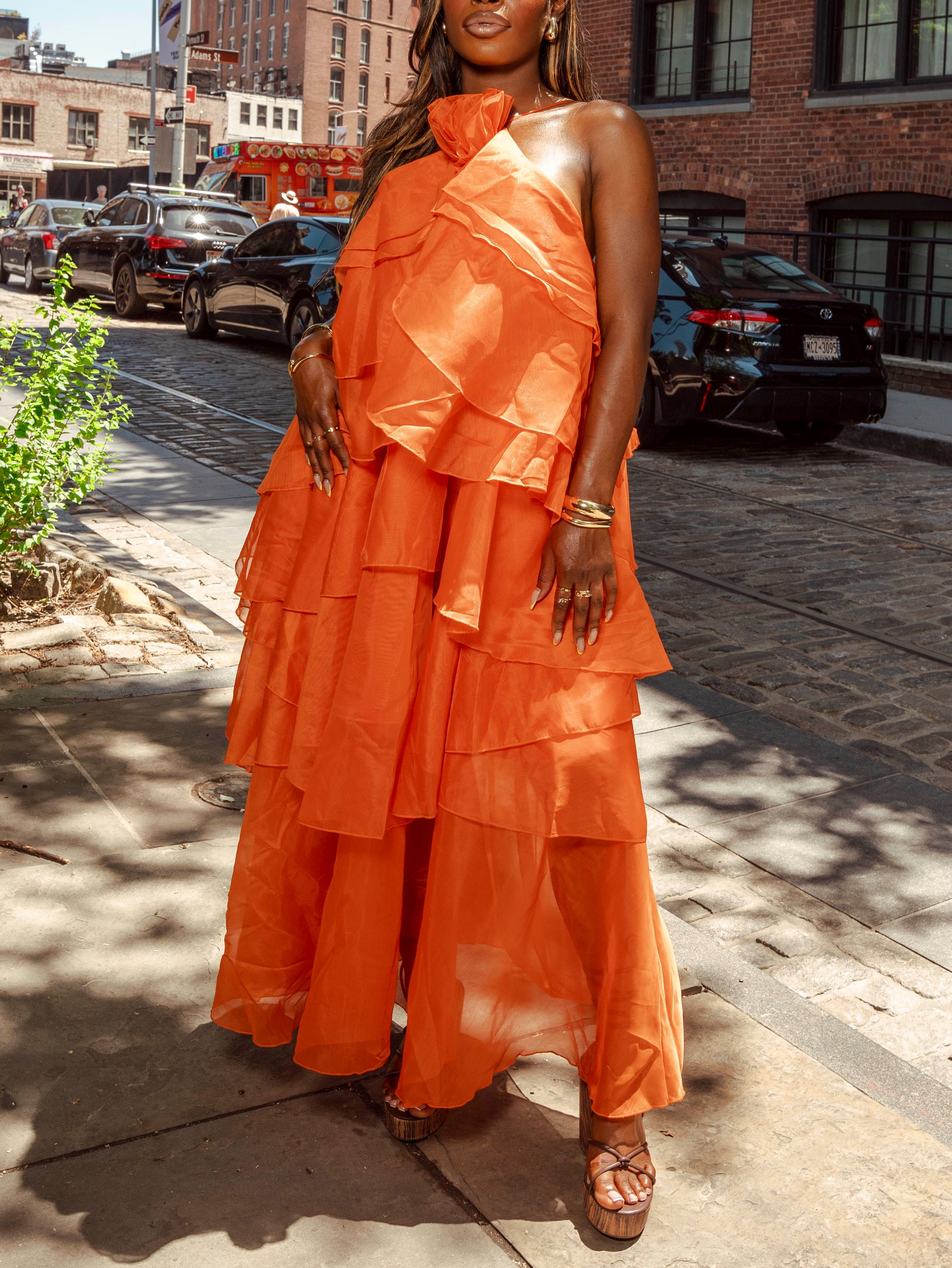 Woman posing in stunning orange halter neck tiered ruffle dress on urban cobblestone street.