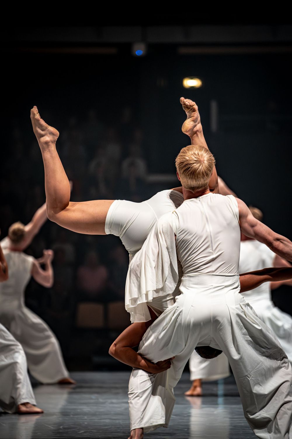 Male dancer lifts partner overhead in white costumes during a contemporary dance performance on stage.
