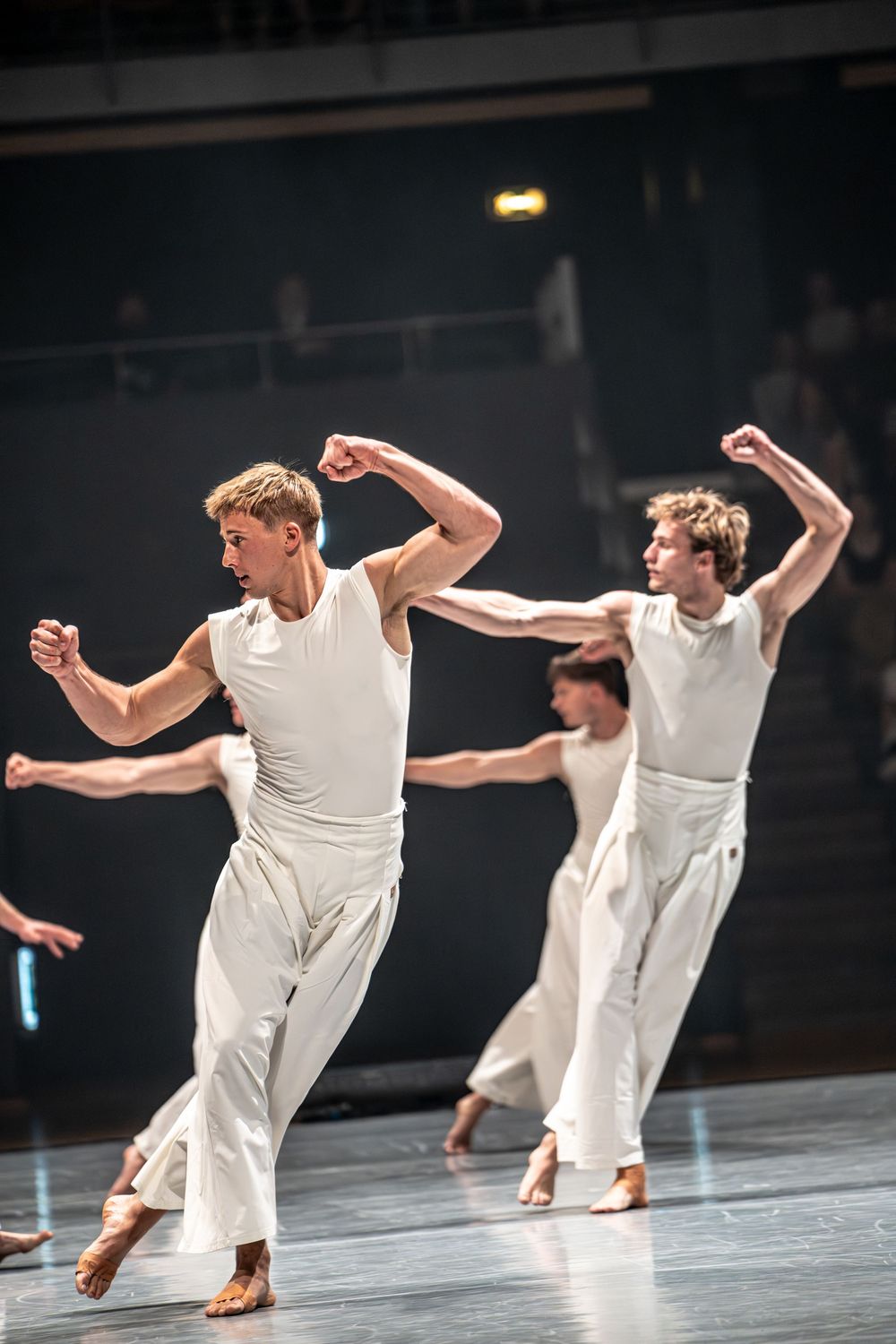 Male contemporary dancers in white costumes perform dynamic choreography on a stage with clenched fists.