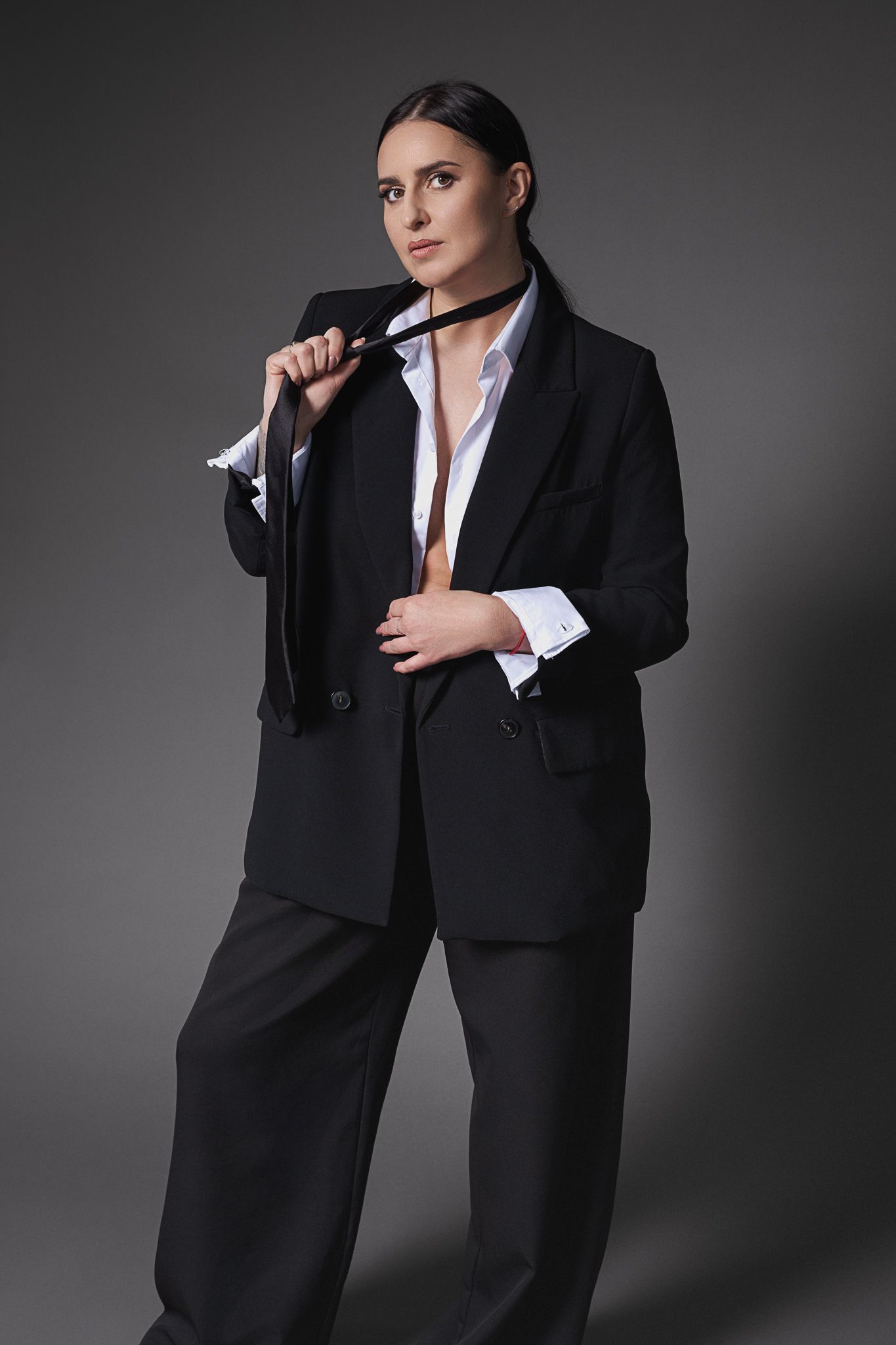 A fashion portrait of a model in an oversized black suit and white shirt against a dark background.