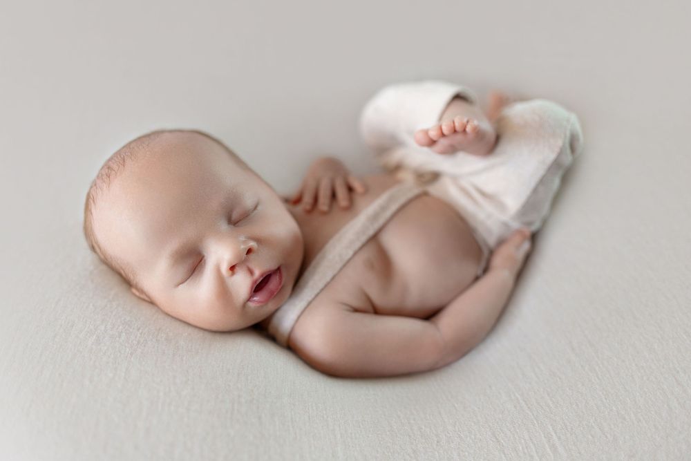 Peaceful newborn baby swaddled in white wrap sleeping on soft cream background in professional studio photo.