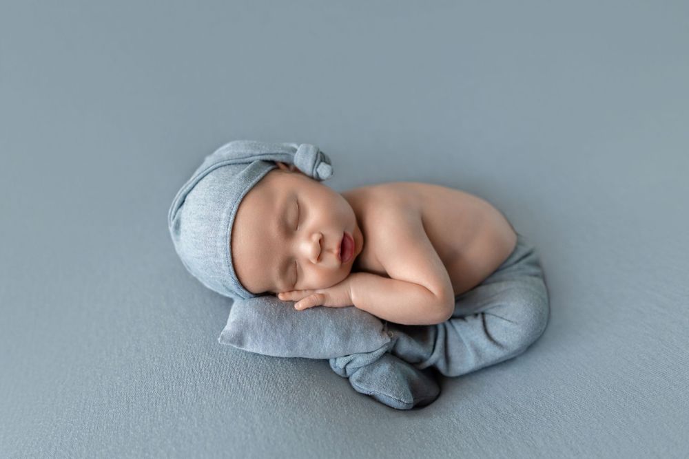 Peaceful newborn baby sleeping in a blue knit hat and wrap on a soft blue blanket in a studio setting.
