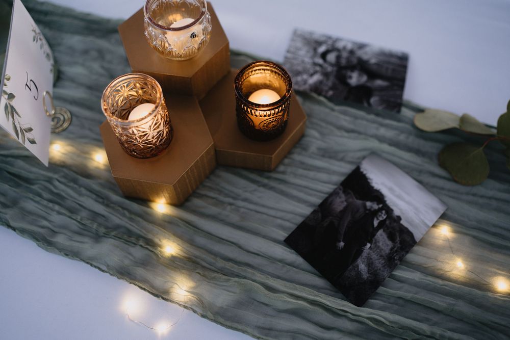 Elegant table display with gold hexagonal candle holders, glowing fairy lights on sage green runner, and black and white photos.