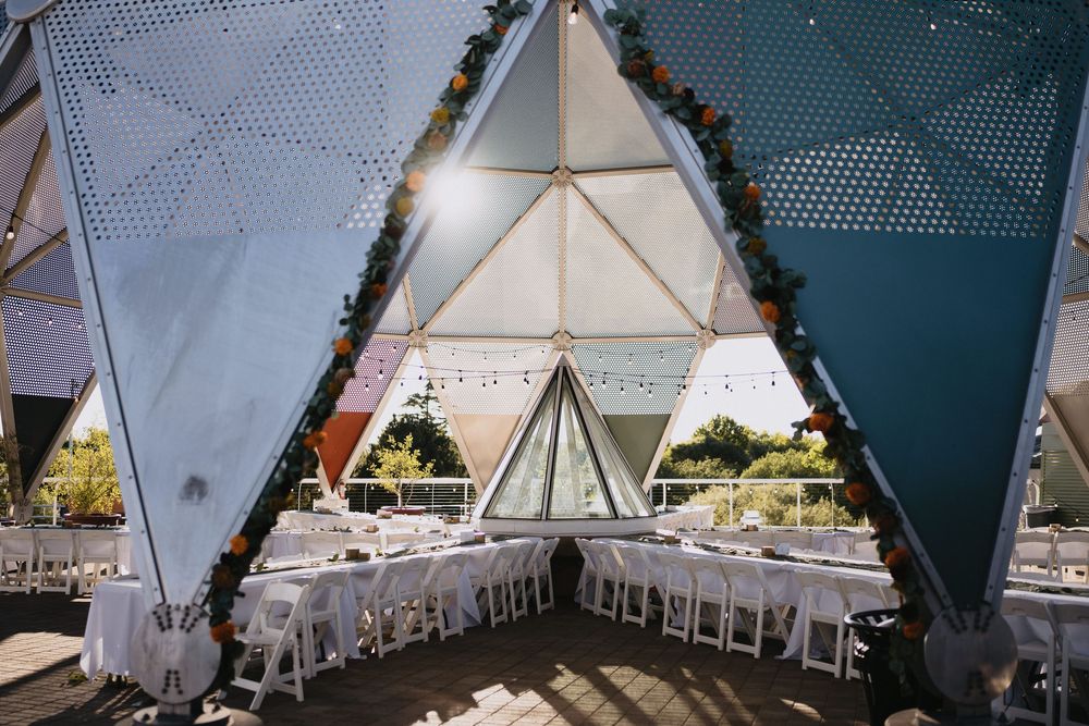 Elegant geodesic dome wedding venue with white dining tables, string lights, and floral garlands under a geometric canopy.