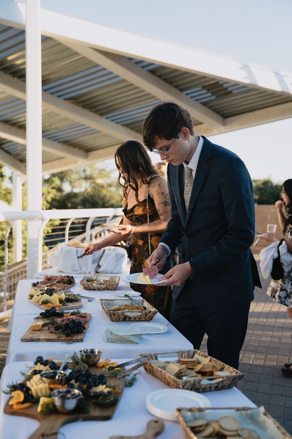 Guests serving themselves at an elegant outdoor wedding reception buffet table with charcuterie and appetizers.
