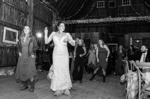 Black and white photo of celebration inside rustic barn with string lights and wooden beams.