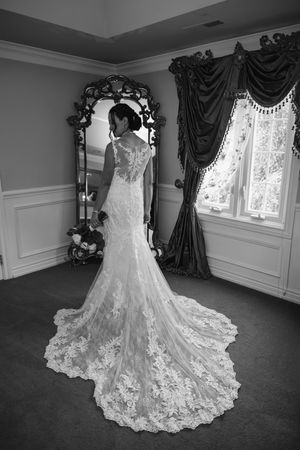 A wedding dress with delicate lace details and long train seen in reflection of an ornate mirror in an elegant room.