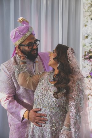 Romantic couple in traditional Indian wedding attire sharing intimate moments against a floral backdrop.