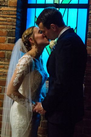 Newlyweds share romantic kiss in front of stained glass window during wedding ceremony.
