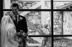 Wedding portrait through window panes with stone wall and carved angel wing detail.
