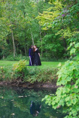 Couple embraces by reflective pond surrounded by lush green forest.