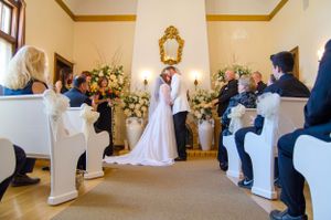 Wedding ceremony in a chapel with white chairs and floral arrangements at the altar.