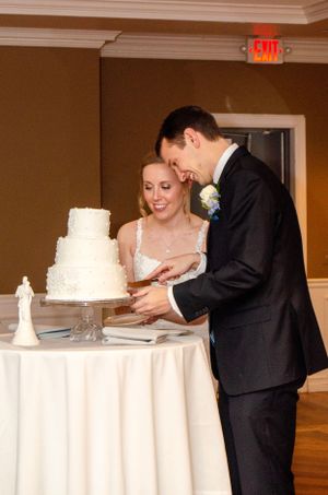 Traditional white three-tier wedding cake cutting moment at an elegant reception.