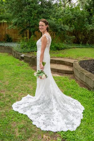 A beautiful white lace wedding dress with a long train spreads across lush green grass in a garden setting.