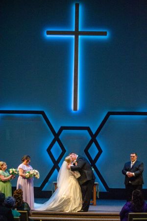 A religious wedding ceremony under a glowing blue cross in a modern church setting.