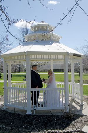 A wedding ceremony taking place in a white gazebo on a sunny spring day.