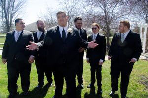 Groomsmen in black suits sharing a lighthearted moment outdoors.