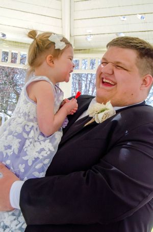 A heartwarming moment between a flower girl in a lavender dress and a groomsman.