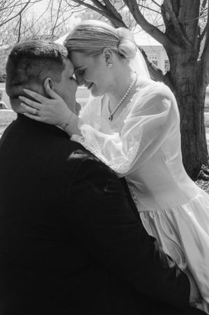 A tender black and white wedding moment between newlyweds sharing a romantic embrace outdoors.