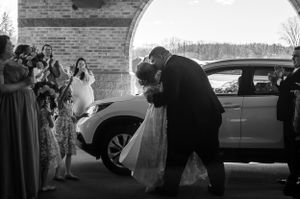 A joyful wedding couple sharing a romantic dip outside their venue as guests look on.