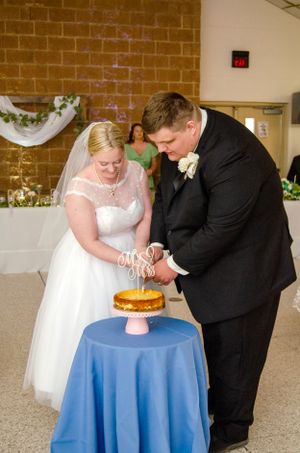 A wedding couple cuts into their celebration cake together on a blue-draped table.
