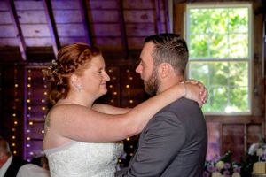 A tender moment between newlyweds dancing in a rustic barn venue with twinkle lights.