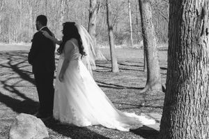A romantic black and white wedding photo of a couple standing among trees in a park.