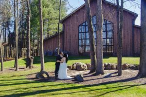 Newlyweds pose in front of a rustic wooden chapel with tall windows surrounded by trees.