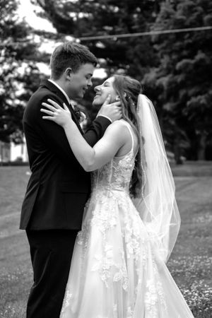 A tender moment between newlyweds in formal attire embracing outdoors.