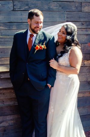 A couple shares a joyful moment at their wedding against a rustic wooden wall background.