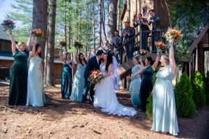 Wedding party poses together in front of tall redwood trees wearing blue and teal dresses.
