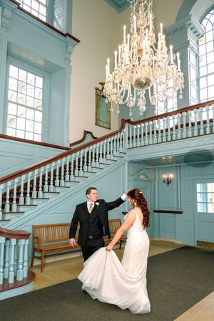 A couple dancing in an elegant venue with a grand crystal chandelier and mint-colored spiral staircase.