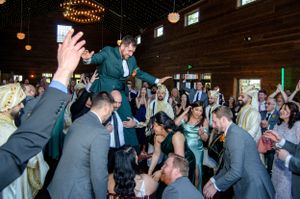 Wedding reception celebration with guests lifting someone up during an energetic dance party.