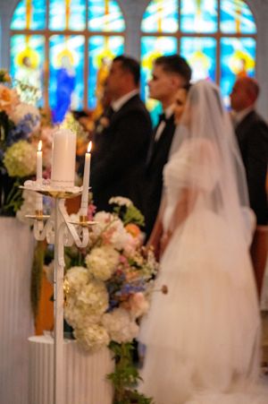 A wedding ceremony scene with stained glass windows and floral arrangements in a church setting.