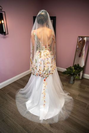 Back view of a bride in a white wedding gown with a flowing veil standing on hardwood floors in a pink room.