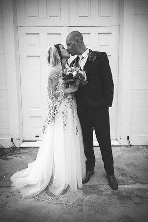 A black and white photo of newlyweds sharing a romantic kiss against a white door.