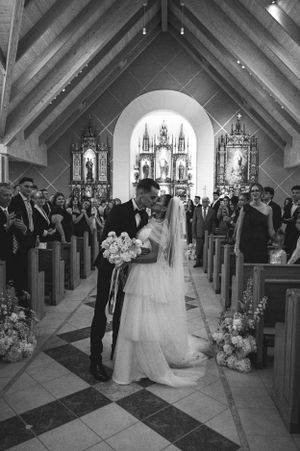 A black and white photograph of a couple in a church aisle during their wedding ceremony.
