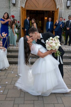 A dramatic wedding kiss captured on church steps surrounded by guests.