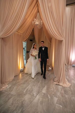A couple walking through an elegant draped entrance with a chandelier at their wedding venue.