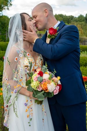 A romantic wedding moment captured in a garden with vibrant coral and yellow floral bouquet details.