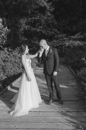 A couple shares a romantic moment on a wooden bridge surrounded by lush greenery during their wedding photoshoot.